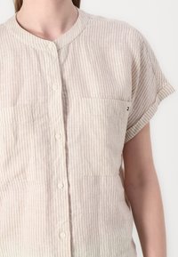 Camicia beige a righe con maniche corte, colletto alla coreana, chiusura con bottoni e due tasche sul petto. Tessuto morbido con una finitura texture.