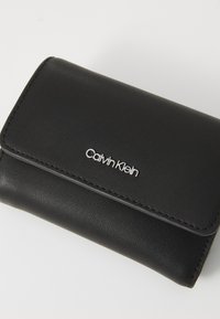 Schwarze Lederbörse mit strukturiertem Finish, Klappen-Design und silbernem "Calvin Klein"-Logo auf der Vorderseite. Kompakter und minimalistischer Stil.