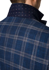 Marynarska kurtka w kratę z teksturowanej tkaniny. Kołnierz wyróżnia się kontrastowym, marynarskim materiałem w małe brązowe kropki. Dopasowany krój.