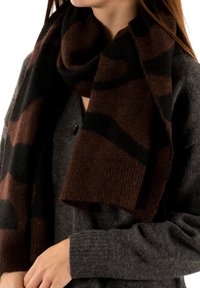 Écharpe en laine à motifs bruns et noirs drapée autour d'un pull gris, avec un bord côtelé et une texture douce. Montre un ajustement confortable autour du cou.