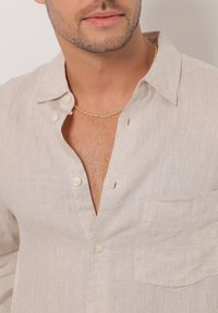Hellbeige Leinenhemd mit lockerer Passform, Button-Down-Kragen, Brusttasche und strukturiertem Stoff. Verfügt über Knöpfe und einen tiefen Ausschnitt.