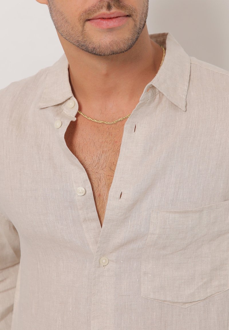 Hellbeige Leinenhemd mit lockerer Passform, Button-Down-Kragen, Brusttasche und strukturiertem Stoff. Verfügt über Knöpfe und einen tiefen Ausschnitt.