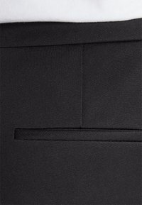 Černé látkové kalhoty s hladkou texturou, jednou zadní kapsou s diskrétní klopou a přesně zpracovanými švy.