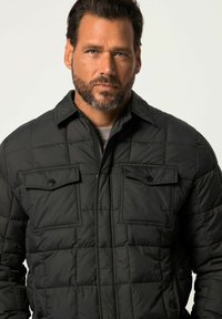 Zwarte gewatteerde jas met knoopsluiting aan de voorkant, twee borstzakken en een kraag. Heeft een zachte, gewatteerde textuur en een slank ontwerp.