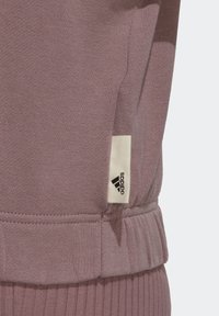 Pantalon de sport mauve clair avec une texture côtelée, équipé d'une taille élastique et d'une petite étiquette blanche adidas avec un logo noir.