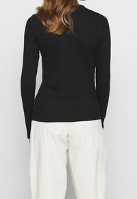 Svart långärmad topp i ribbat material, åtsittande design. Matchad med off-white, avslappnade byxor med bakfickor.