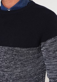 Sweter dziewiarski z granatową górną częścią, przechodzącą w teksturowaną dolną część w szaro-białe wzory. Okrągły dekolt i ściągacze.