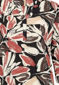 Zwarte blouse met een bloemenpatroon in rode, beige en bruine kwaststrepen; bevat een uitsparing kraag en korte mouwen.