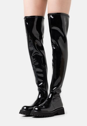 Botas de charol negras hasta la rodilla con un acabado brillante, suelas de goma audaces y un diseño elegante que incluye un cierre de cremallera en el costado.