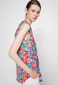 Blusa sem mangas colorida com um padrão floral em vermelho, azul e verde. Tecido leve com um corte solto e bainha arredondada.