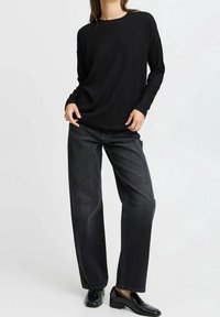 Schwarzes, geripptes Langarmoberteil, kombiniert mit hoch taillierten, weiten, dunklen Jeans, ergänzt durch glänzende schwarze Slipper.