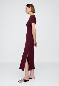 Robe bordeaux longueur cheville en tissu doux, avec des manches courtes, une silhouette ajustée et des fentes latérales hautes pour faciliter les mouvements.