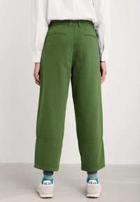 Gröna vida byxor med hög midja, två bakfickor och en jämn textur, tillsammans med vita sneakers och flerfärgade strumpor.