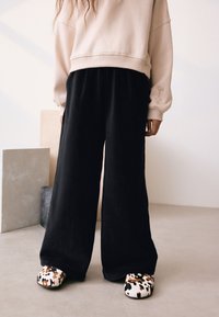 Crne široke hlače, uparene s kremastom dugom majicom s vezom, i mekane cipele na navlačenje s smeđim i bijelim leopardovim uzorkom.