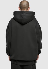Felpa nera oversize con cappuccio prominente, realizzata in tessuto morbido. Presenta spalle scese e una vestibilità ampia, senza loghi visibili.