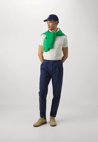 Λευκό πόλο πουκάμισο, πράσινο πουλόβερ δεμένο γύρω από τον λαιμό, μπλε παντελόνι και καφέ αθλητικά παπούτσια με κόκκινες λεπτομέρειες. Μπλε καπέλο ολοκληρώνει το ντύσιμο.