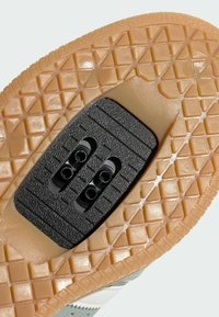 Kenkäpohja, jossa on hunajanvärinen kumipinta ja musta, teksturoitu klippialue. Ominaisuuksiin kuuluu timanttimäinen kuvio, joka tarjoaa pitoa ja vakautta.