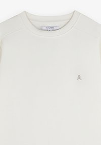 Sudadera color crema hecha de tela suave, con un cuello redondo, mangas raglán y un pequeño logo de calavera plateada en el pecho.