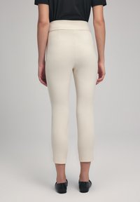 Beige skräddarsydda byxor med hög midja, smal passform och kort längd. Tyget verkar slätt med en lätt glans.