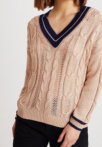 Maglione lavorato a maglia in rosa chiaro con motivo a trecce, dotato di un profondo scollo a V blu navy e polsini in contrasto blu navy. Orlo a costine e materiale testurizzato.