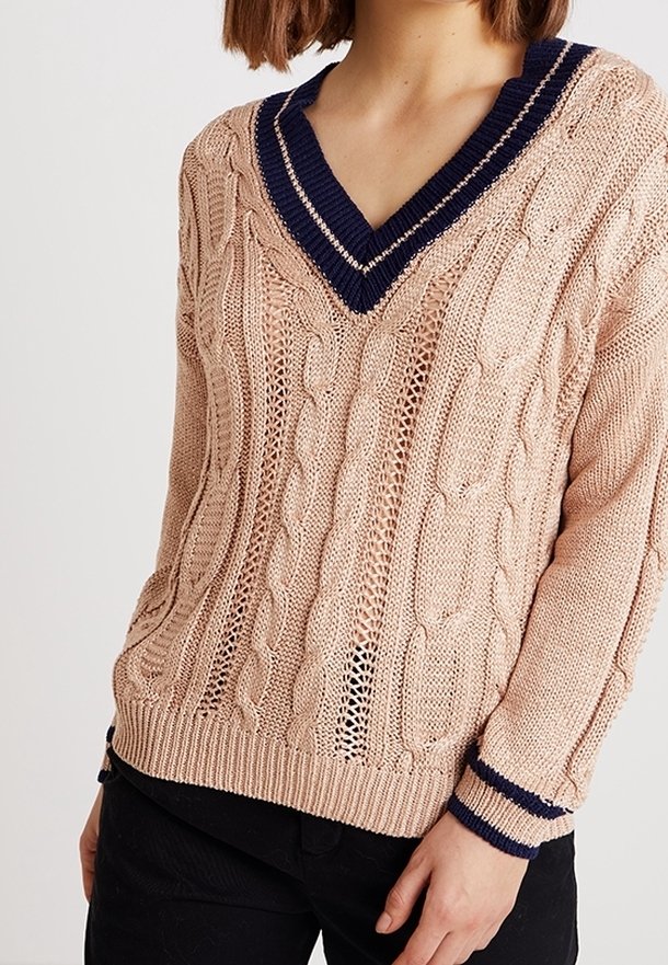 Maglione lavorato a maglia in rosa chiaro con motivo a trecce, dotato di un profondo scollo a V blu navy e polsini in contrasto blu navy. Orlo a costine e materiale testurizzato.