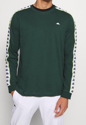 Camisa verde de manga larga en una mezcla de algodón con franjas laterales en blanco y negro contrastantes, que presenta un pequeño logo en el pecho.