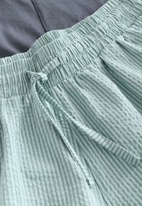 Shorts en tissu rayé bleu sarcelle clair avec une taille élastique et un cordon ajustable, présentant une texture froissée.