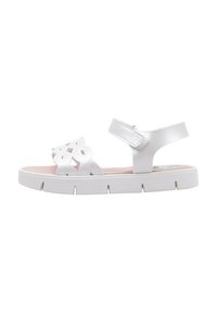 Sandalia blanca con diseño recortado en las correas y correa ajustable en el tobillo, que presenta una gruesa suela blanca y una plantilla rosa.