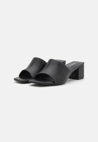 Black leather block-heeled mules feature an open-toe design and wide instep straps, with a smooth texture and minimalist aesthetic.