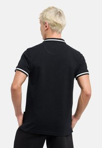 Sort polo-shirt med hvide stribede detaljer på kraven og ærmerne, lavet af bomuld, med en afslappet pasform og en glat tekstur.