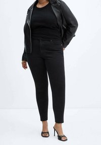 Vaqueros de mezclilla negros de corte slim, combinados con una blusa negra ajustada y una chaqueta de cuero. Sandalias altas negras completan el look.