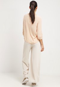 Ljus persiko, långärmad blus med texturerad tyg och rundad nederkant, matchad med löst sittande, krämfärgade vida byxor och ljusa sneakers.