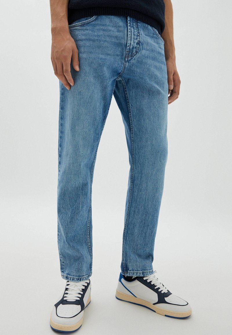 Ljust blå denimjeans med rak benform, med kontrasterande sömmar, fem fickor och en lätt blekning. Kombinerat med vita och marinblå sneakers.