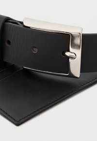 Μαύρη δερμάτινη ζώνη με υφασμένο πυκνό μοτίβο, ασημένια μεταλλική αγκράφα και αρκετές τρύπες για προσαρμογή. Οι ραμμένες άκρες ενισχύουν την ανθεκτικότητα.