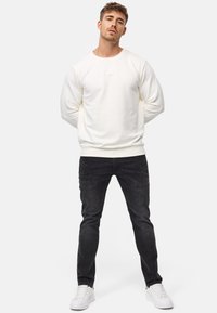 Vit bomulls sweatshirt med rund hals, med en liten logopatch. Kombinerad med mörk denimjeans och vita sneakers.