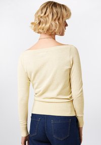 Gelbes schulterfreies Sweatshirt mit langen Ärmeln, geripptem Saum und weicher Textur. Getragen mit dunkelblauen Jeans, von hinten betrachtet.