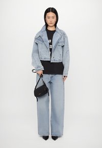 Svijetloplavi skraćeni traper jakna s velikim džepovima, crni majica s grafikom, široke svijetloplave traperice i mala crna torbica preko ramena.