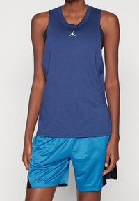 Granatowa koszulka bez rękawów z okrągłym dekoltem i białym logo. Połączona z jasnoniebieskimi szortami sportowymi z siateczki z czarnymi akcentami.