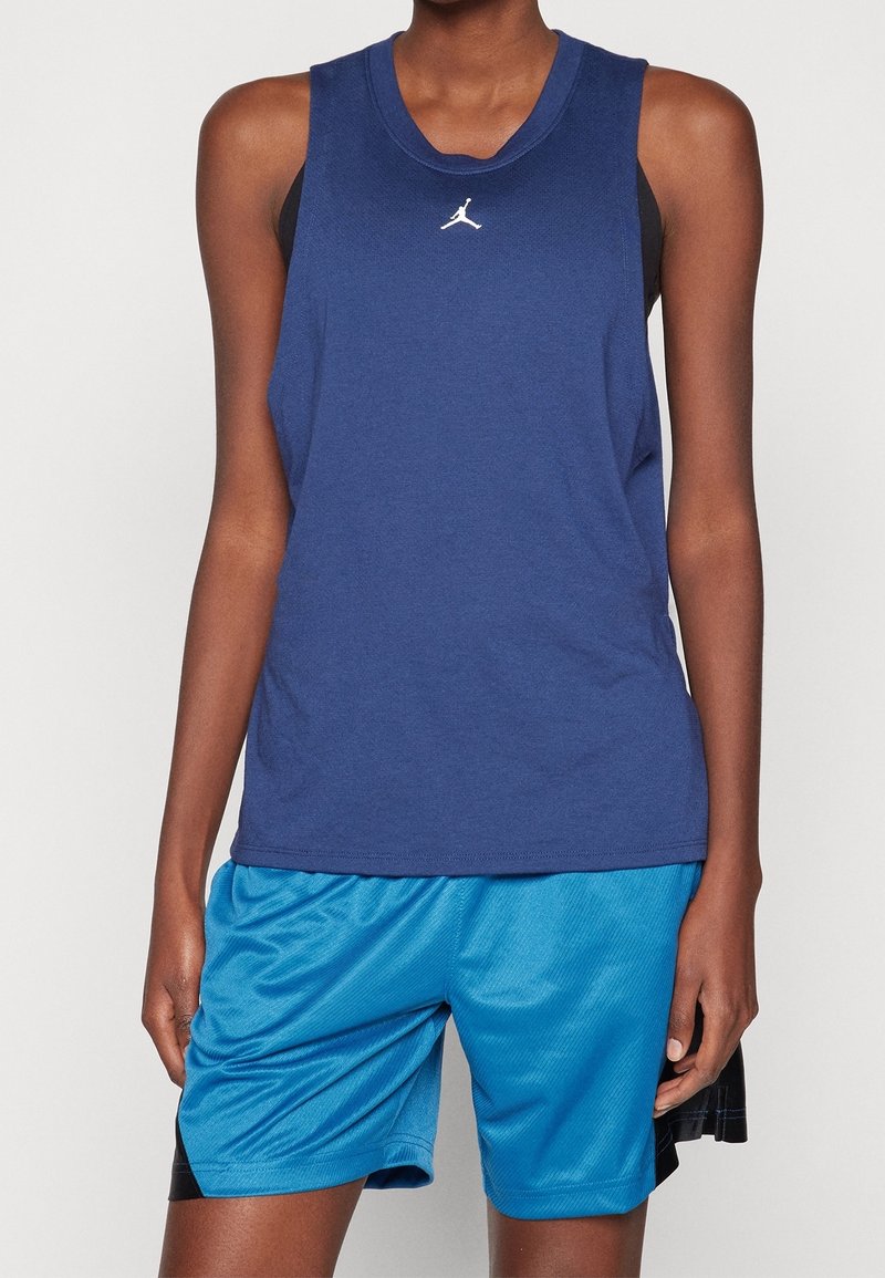 Granatowa koszulka bez rękawów z okrągłym dekoltem i białym logo. Połączona z jasnoniebieskimi szortami sportowymi z siateczki z czarnymi akcentami.