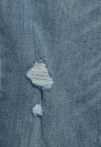 Tejido de mezclilla azul claro con una área desgastada que muestra un desgarro. La textura es típica de la mezclilla, con un sutil tejido y bordes deshilachados.