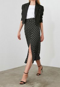 Falda de lunares en blanco y negro con una abertura lateral, combinada con una chaqueta negra ajustada y una camiseta gráfica blanca. Tacones negros con tiras.