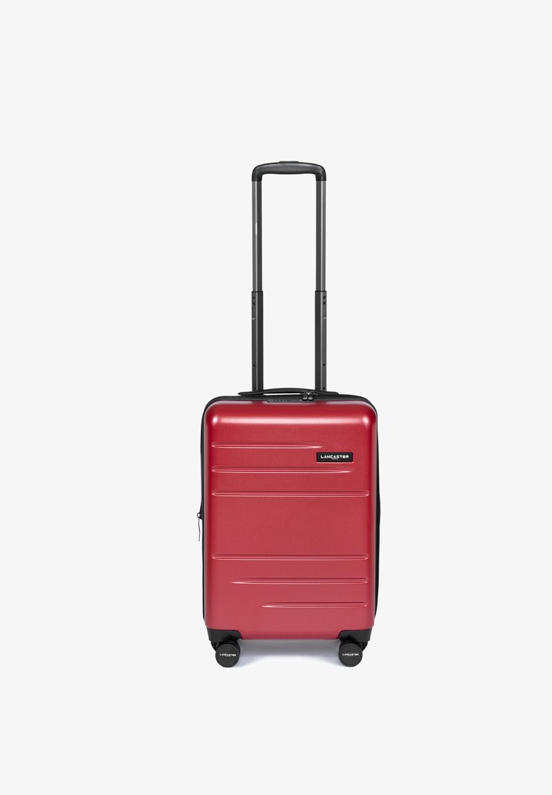 Valigia rigida rossa dal design elegante, con scanalature verticali, dettagli neri, manico estraibile e quattro ruote per la mobilità.