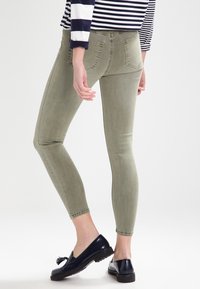 Jeans ajustados en verde oliva, con una cintura de altura media, diseño de cinco bolsillos y un desvanecido sutil, combinados con mocasines negros.