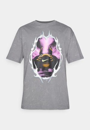 Grå bomulds-T-shirt med et centralt grafisk motiv af en person, der holder en bold, omgivet af lilla og hvide flamme-lignende design.