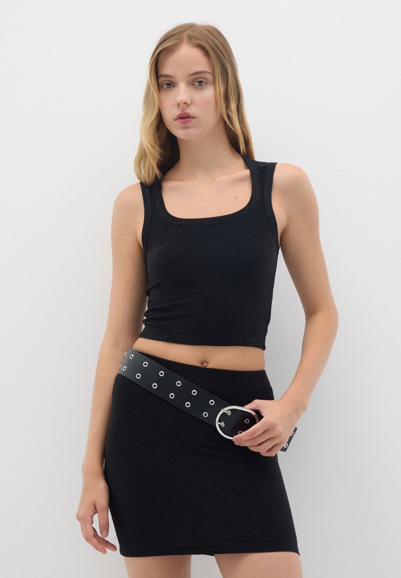 Un débardeur noir ajusté avec un col carré, associé à une mini-jupe assortie. L'ensemble est complété par une large ceinture noire avec des œillets en argent.