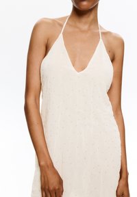 Abito halter color crema con profondo scollo a V, caratterizzato da un delicato motivo testurizzato e piccoli embellishments circolari sparsi.