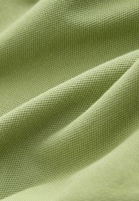 Vaaleanvihreä, kuvioitu kangas, jossa ruudukon kaltainen kuvio ja pehmeä laskostus, viitaten kudottuun tekstiiliin, joka sopii vaatteisiin tai verhoiluun.