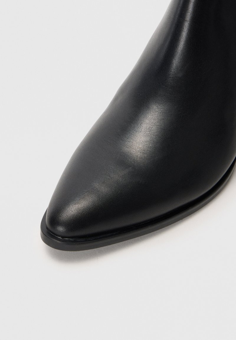 Bottine en cuir noir avec un bout pointu et une texture lisse. Présente un éclat subtil et une semelle plate fine pour un minimum d'élévation.