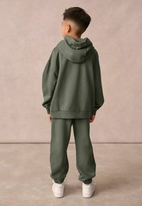 Zestaw bluzy z kapturem i spodni dresowych w oliwkowym kolorze, wykonany z miękkiego materiału. Bluza ma kaptur ze sznurkiem, a dresy mają elastyczne mankiety i luźny krój.