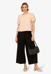 Top texturizzato rosa chiaro con maniche a sbuffo corte, abbinato a pantaloni neri a gamba larga e una borsa nera. Scarpe con tacco a blocco beige.